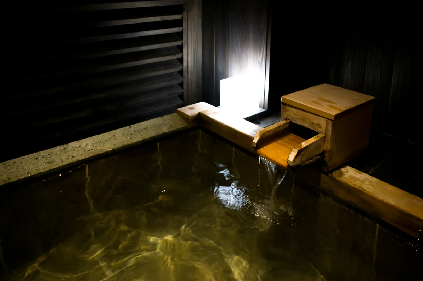 暗い石造りの湯船に湯を注ぐ木の湯口