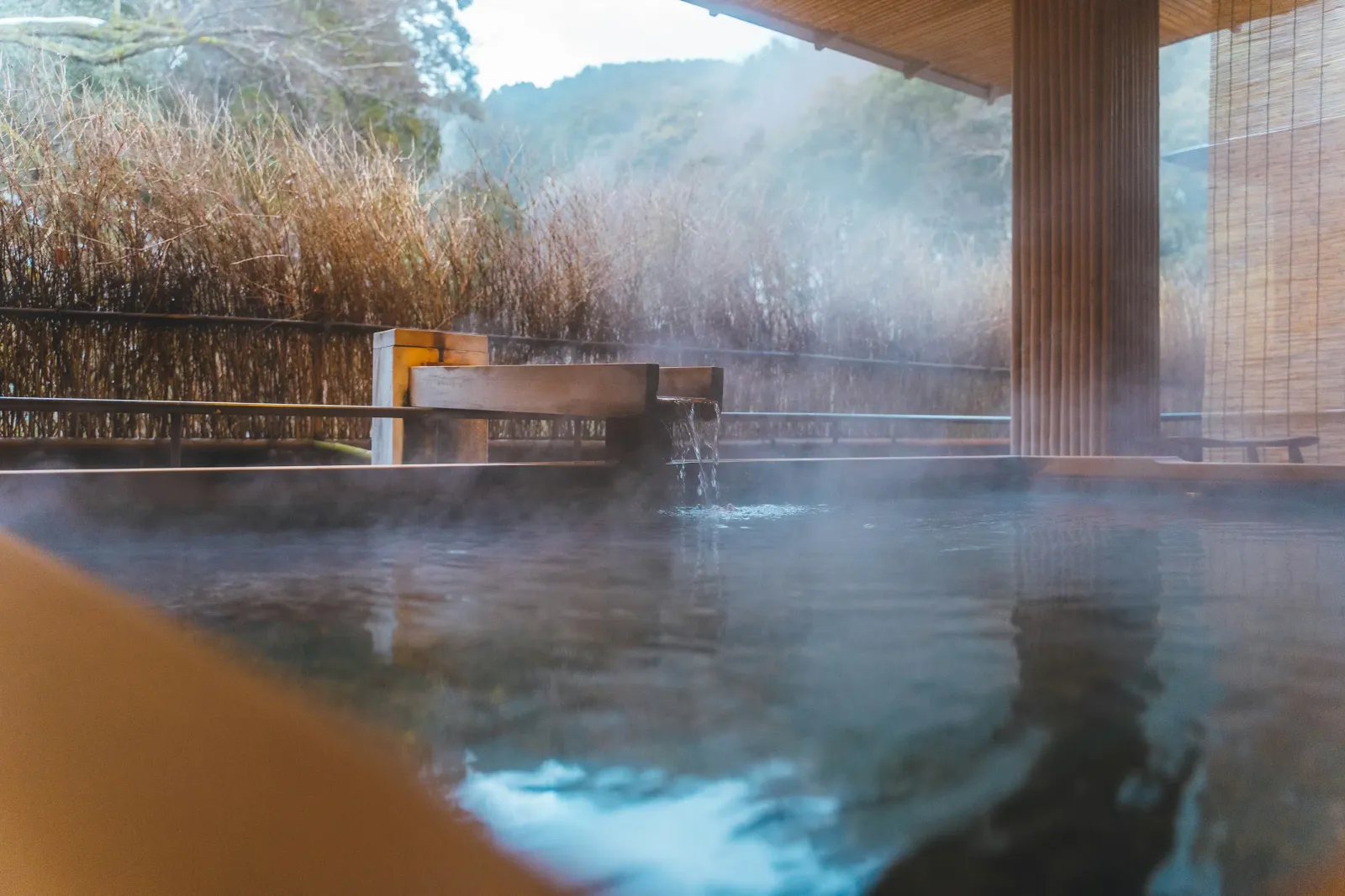 湯気の立つ露天風呂と、竹垣の向こうに広がる山並み